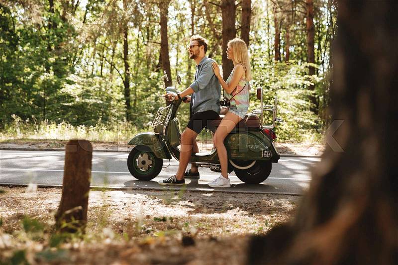 Image of young bearded man on scooter with happy girlfriend outdoors. Looking aside, stock photo