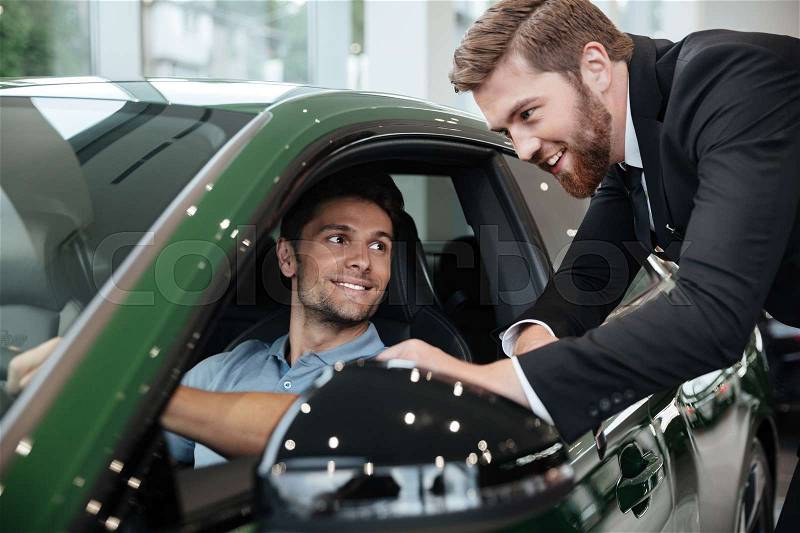 Professional male dealer selling car to a customer at the dealership, stock photo