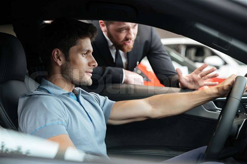 Professional young male dealer selling car to a customer at the dealership, stock photo