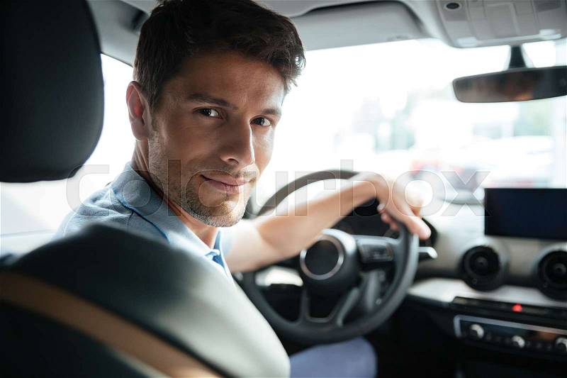 Handsome smiling male customer testing his new car at the dealership, stock photo