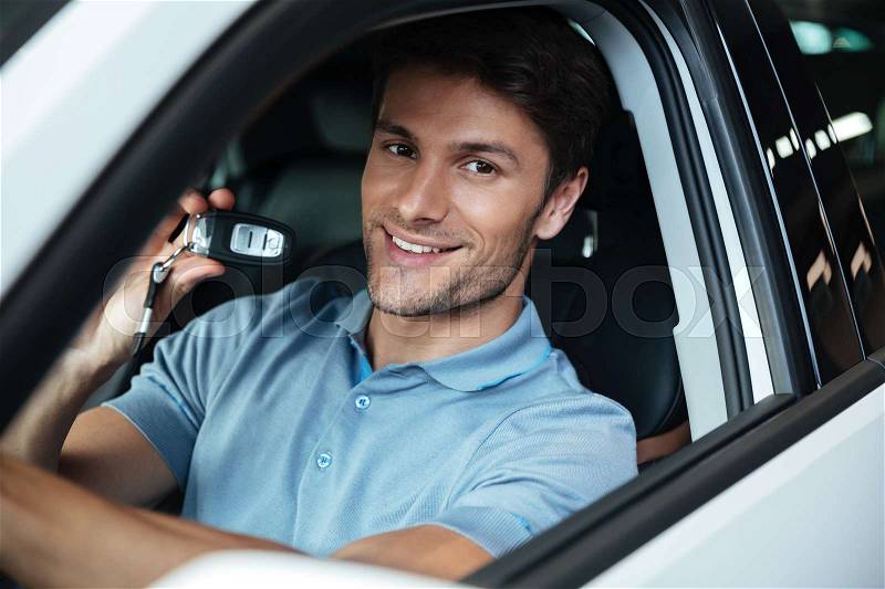 Handsome happy man sitting in his new car and showing car keys at the dealership, stock photo