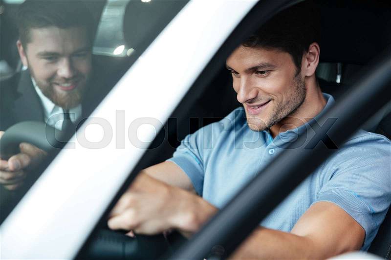 Young smiling couple testing a new car while sitting inside with a dealer, stock photo