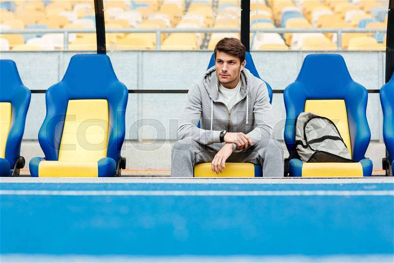 Young male athlete in sportswear sitting on a stadium seats and waiting for his coach, stock photo