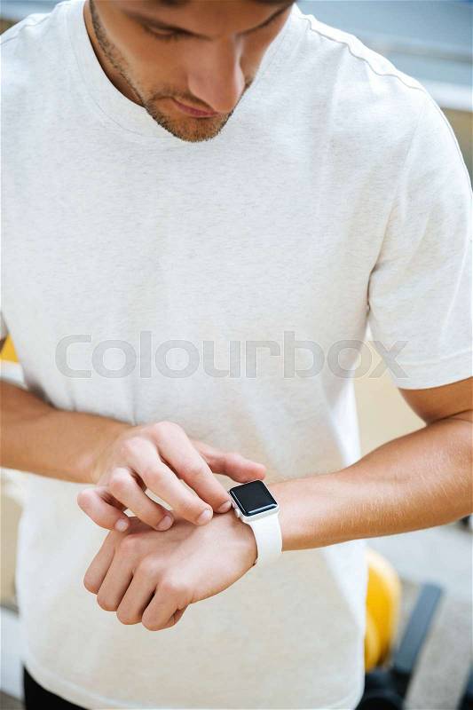 Picture of concentrated young sports man looking at watch at the stadium outdoors, stock photo
