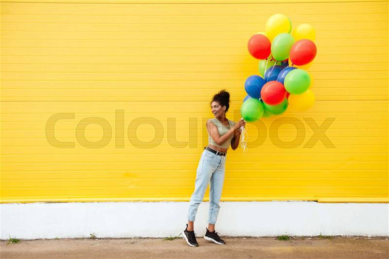 Image of young happy african woman standing over yellow wall. Have fun with balloons, stock photo