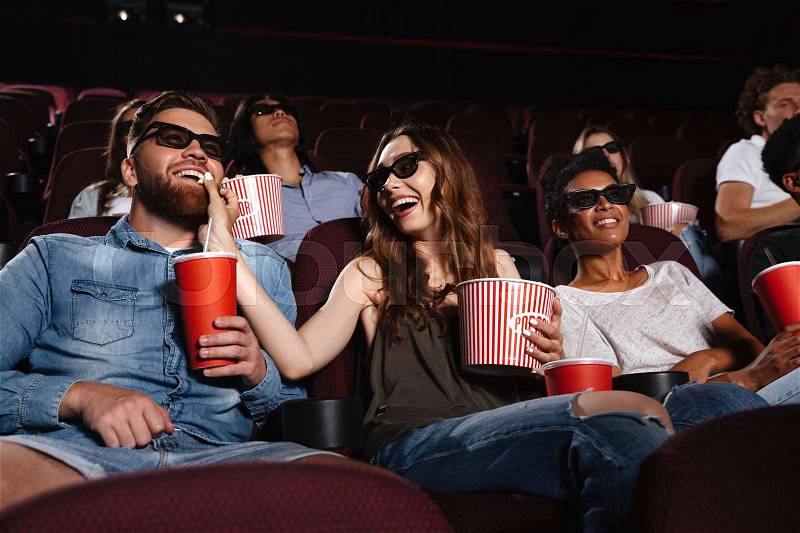 Photo of happy friends sitting in cinema watch film eating popcorn and drinking aerated sweet water, stock photo