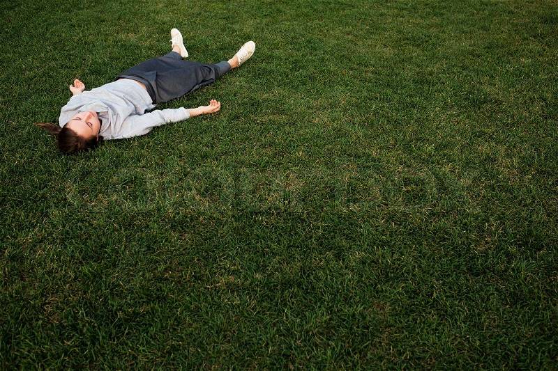 Beautiful young european woman lays down on grass and rests in summer day, stock photo