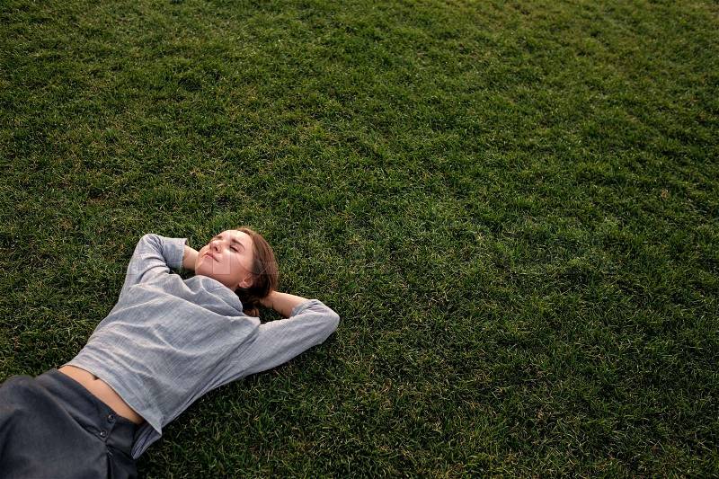 Beautiful young european woman lays down on grass and rests in summer day, stock photo