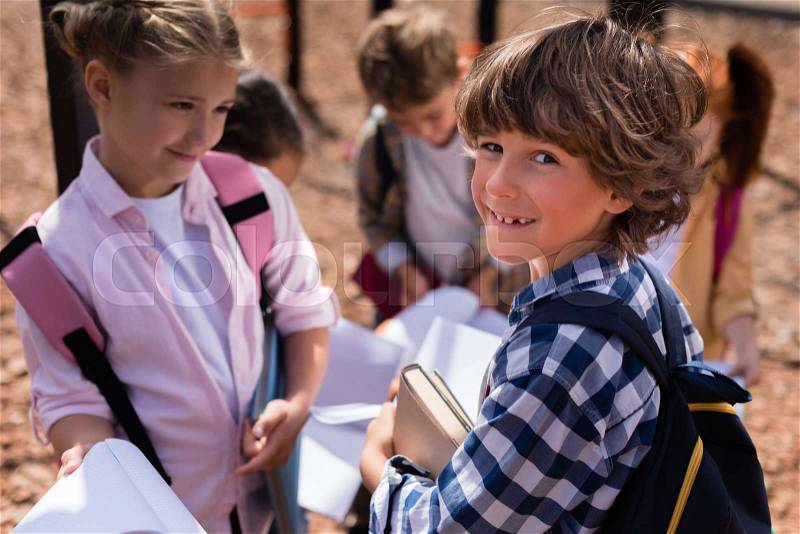 Cute happy schoolkids holding books and smiling at camera on playground, stock photo