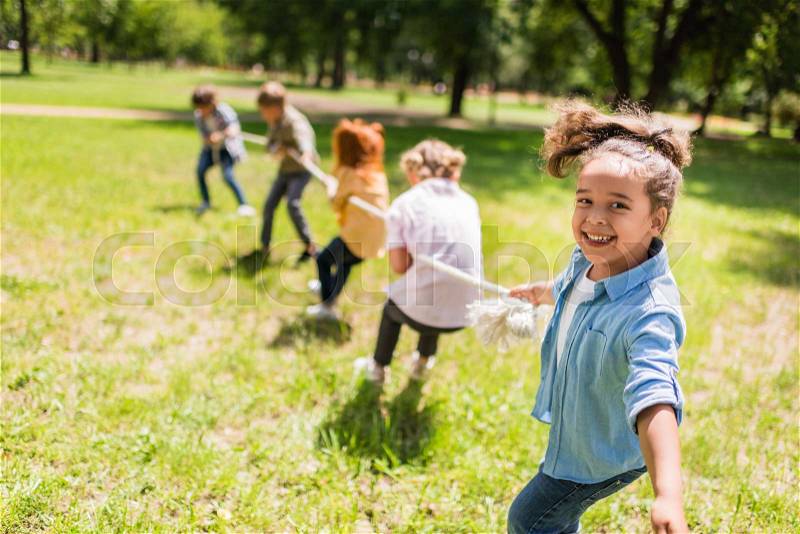 Happy multiethnic kids playing tug of war in park, stock photo
