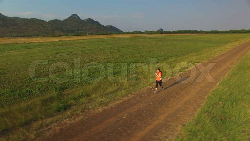 Aerial view of woman running on a rural road during sunset in the mountains, stock photo
