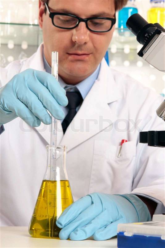 Scientist using a stirrer to mix liquids in flaskFocus to hands and science labware, stock photo