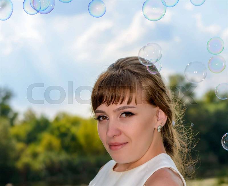 Pretty young bride watching floating soap bubbles wafting in the air as she dreams of new beginnings in her future life, stock photo
