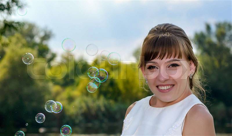 Pretty young bride watching floating soap bubbles wafting in the air as she dreams of new beginnings in her future life, stock photo