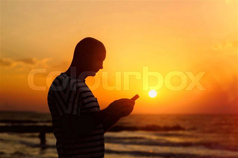 Man with phone in the background of the setting sun, stock photo