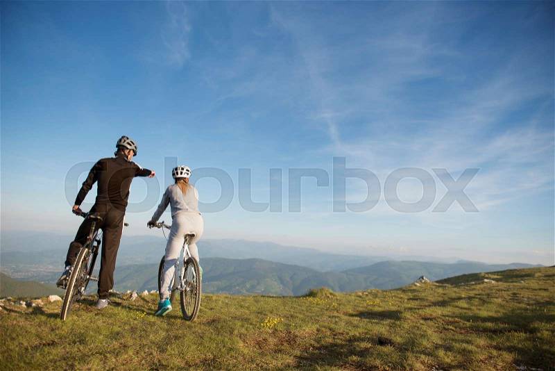 Biker couple with mountain bike pointing in distance at countryside, stock photo