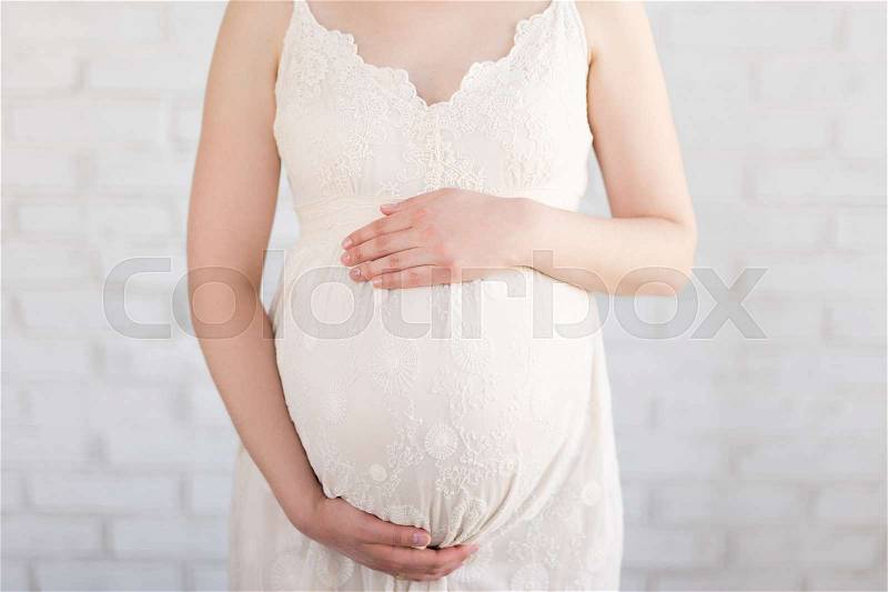 Pregnancy concept - close up of pregnant belly over white brick wall, stock photo