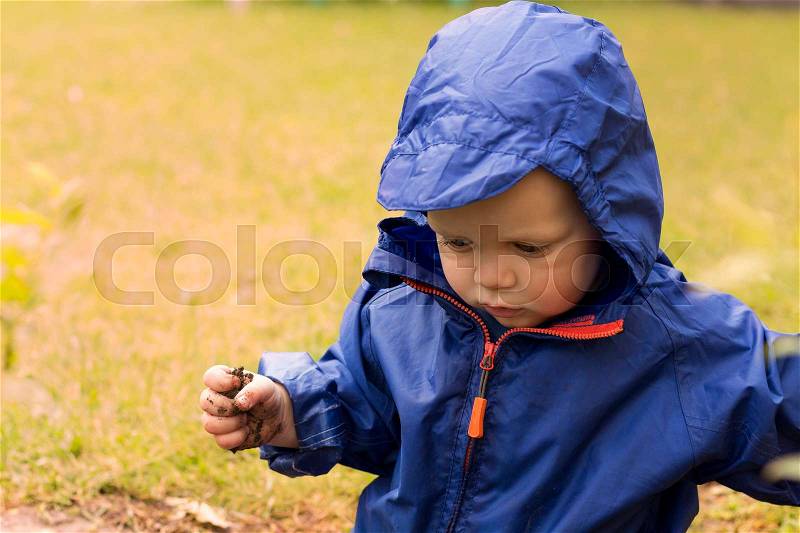 Happy toddler in a blue raincoat against blurred grass. Autumn concept. Copy space, stock photo