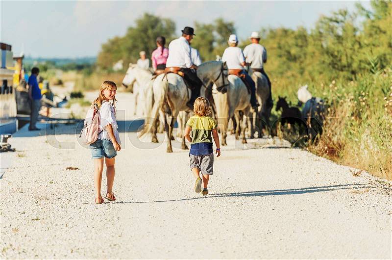 Kids tourists enjoying a trip to South of France, white wild horse in Parc Regional de Camargue - Provence, stock photo
