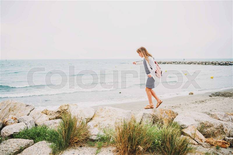 Little girl enjoying summer vacation by the sea, wearing stripe nautical dress and backpack. Image taken in Saintes-Maries-de-la-Mer, capital of Camargue, south of France, stock photo