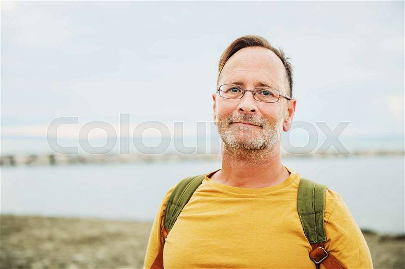 Handsome man on summer vacation by the sea, wearing yellow safran t-shirt and backpack, stock photo