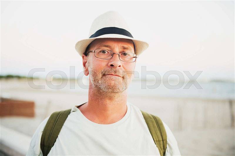 Handsome man on summer vacation by the sea, wearing hat, glasses and backpack, stock photo