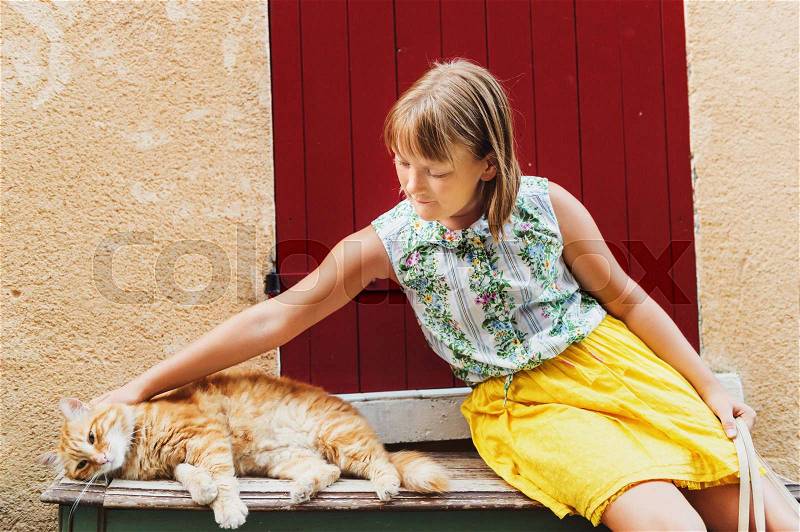 Cute little girl playing with furry ginger cat outside. Image taken in Valensole, Alpes-de-Haute-Provence department, France, stock photo