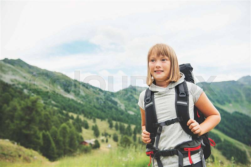 Happy little girl hiking in swiss Alps, wearing black backpack, travel with kids. Image taken in canton of Valais, Switzerland, stock photo