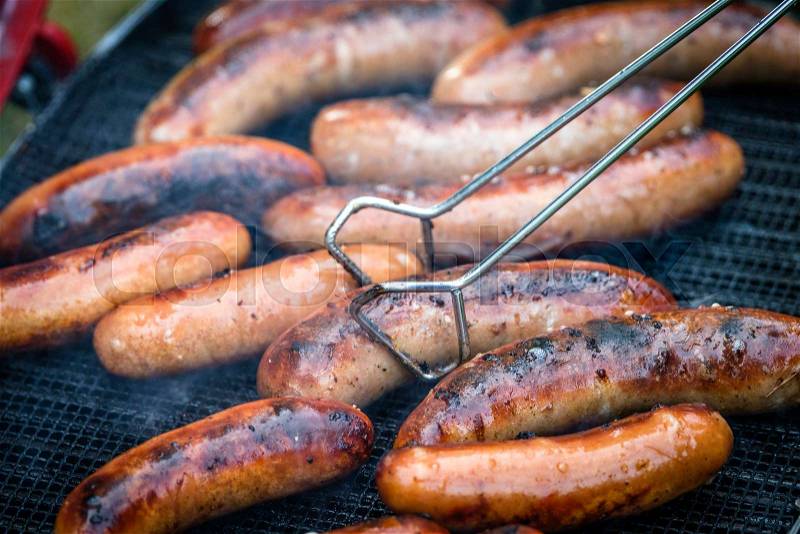 Crispy wieners on an outdoor grill in the summer with a sausages plier in metal, stock photo