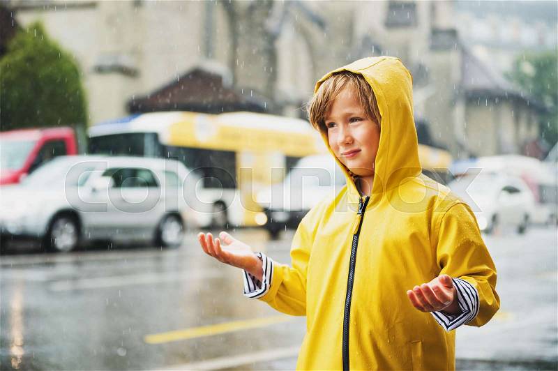 Cute little boy playing under the rain in a city, wearing bright yellow raincoat with hood. Image taken in Saint-Francois square, Lausanne, Switzerland, stock photo