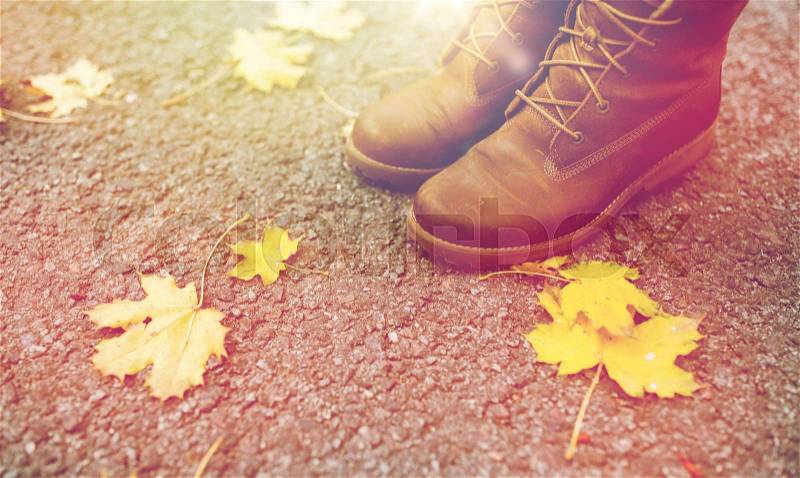 Season, footwear and people concept - female feet in boots with autumn leaves on ground, stock photo