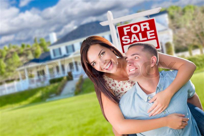 Playful Excited Military Couple In Front of Home with For Sale Real Estate Sign, stock photo