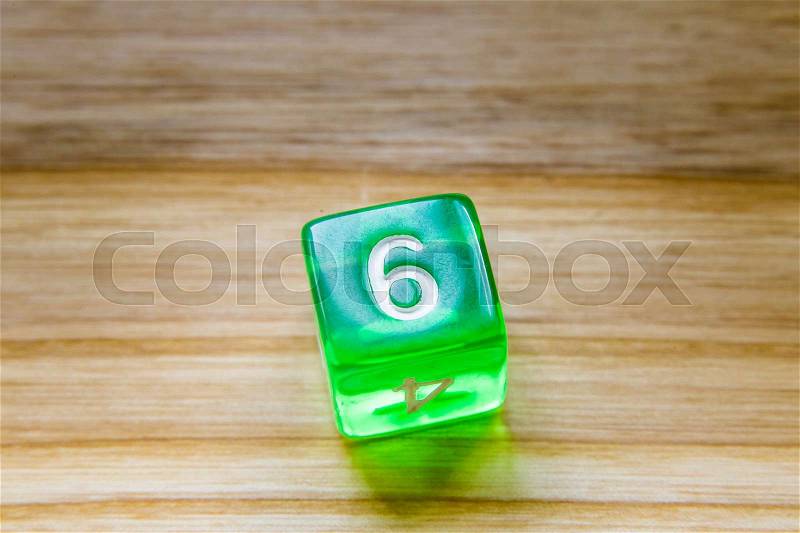 A translucent green six sided playing dice on a wooden background with number six on a top, stock photo