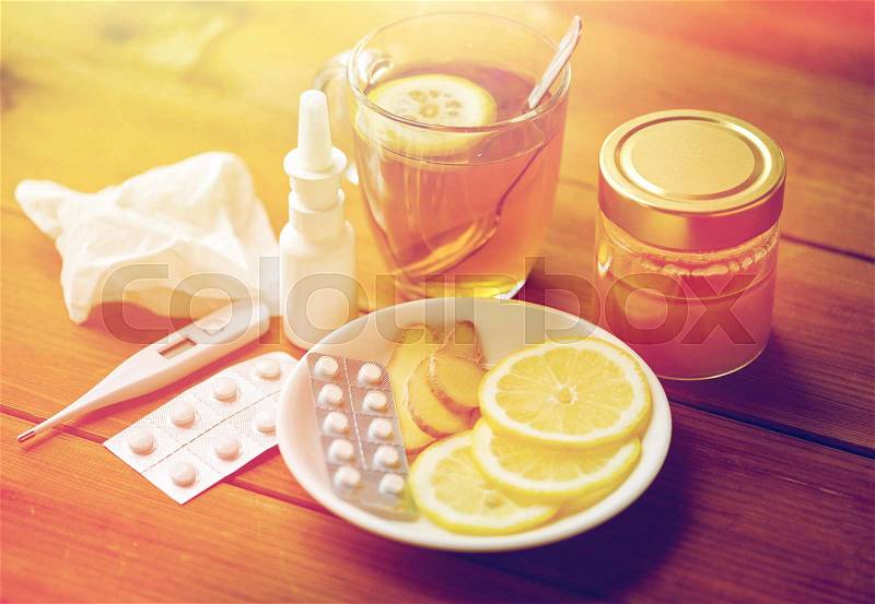 Healthcare, traditional medicine and flu concept - tea cup with lemon, ginger, honey and pills on wooden table, stock photo