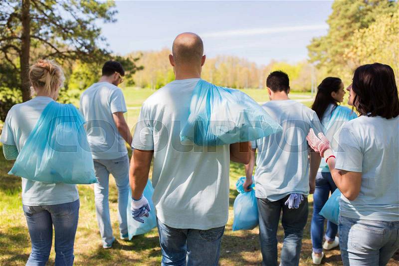 Volunteering, people and ecology concept - group of happy volunteers with garbage bags walking after cleaning park area, stock photo