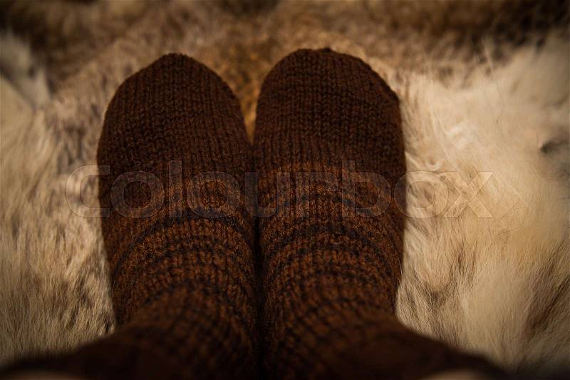 Warm hand knitted woolen socks on a fur background. First person view, stock photo