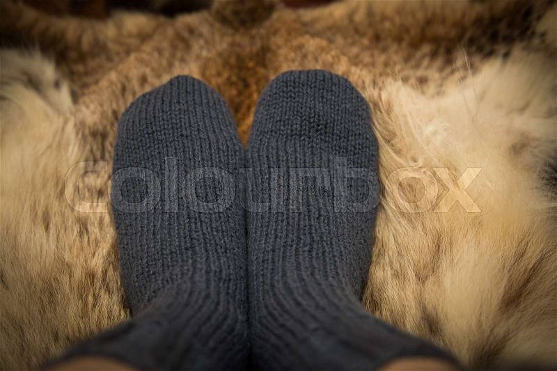 Warm hand knitted woolen socks on a fur background. First person view, stock photo