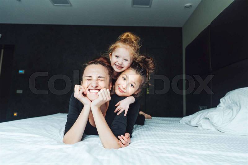 Mom and two daughters have fun on the bed in the bedroom, stock photo