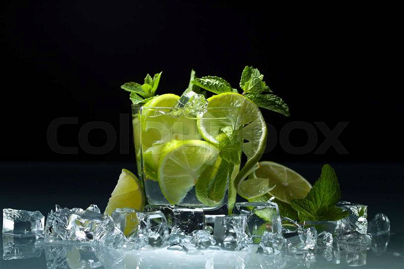 Cocktail with lime , ice and peppermint leaves on a glass table in bar. Black background , stock photo