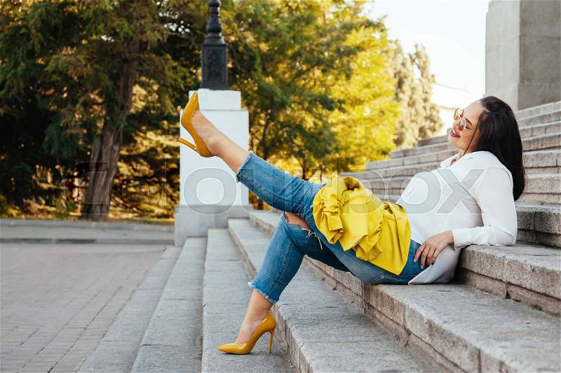 Prerry young woman wearing bright colorful jacket, ripped jeans and heel shoes walking on the city street. Casual fashion, plus size model, stock photo