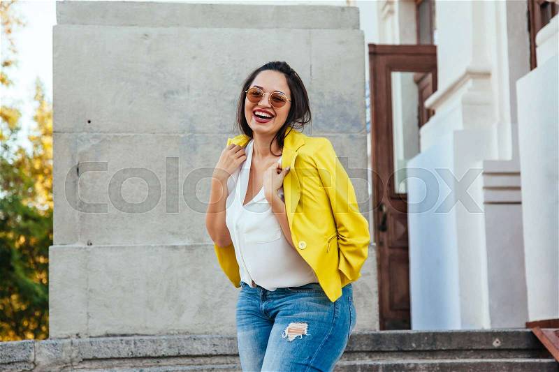 Pretty young woman wearing bright colorful jacket walking on the city street. Casual fashion, plus size model, stock photo