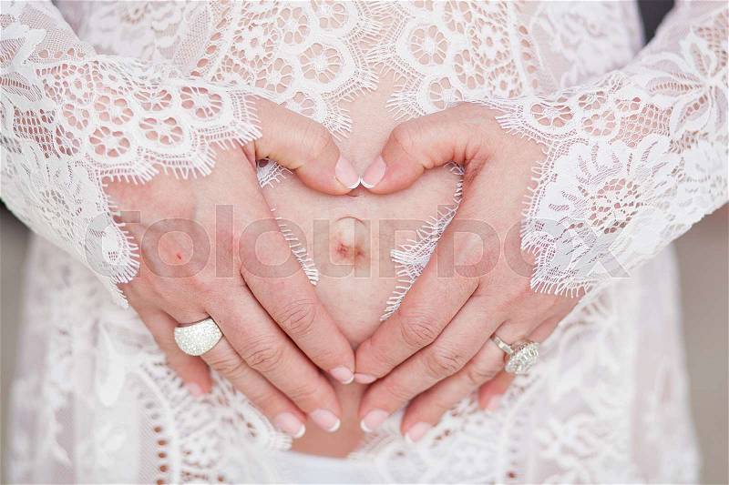 A woman hugging a lovely pregnant tummy. Hands in the shape of a heart. Beautiful delicate lingerie, stock photo