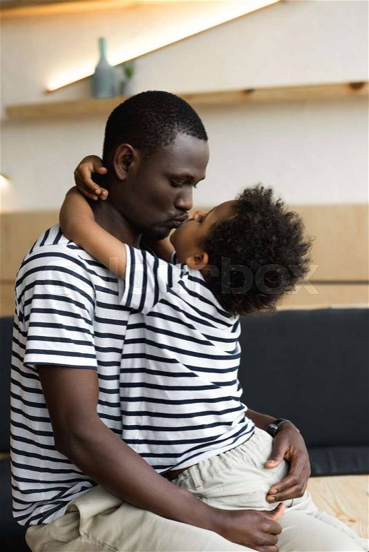 Happy african american father and son hugging and kissing together, stock photo
