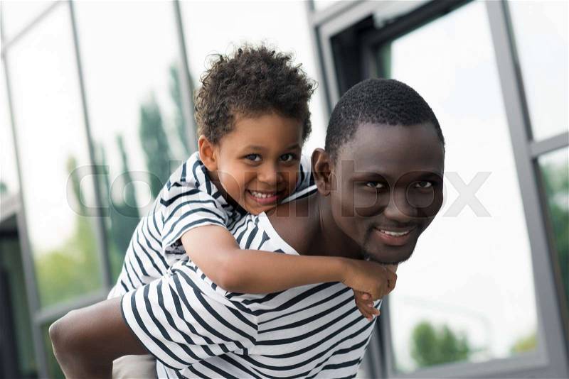 Happy african american father piggybacking son and smiling at camera, stock photo