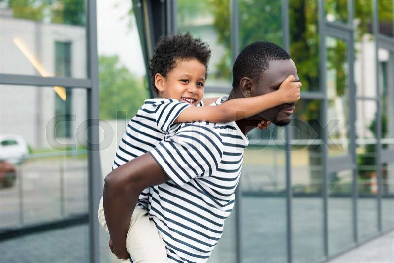 Side view of young african american father piggybacking cute smiling son, stock photo