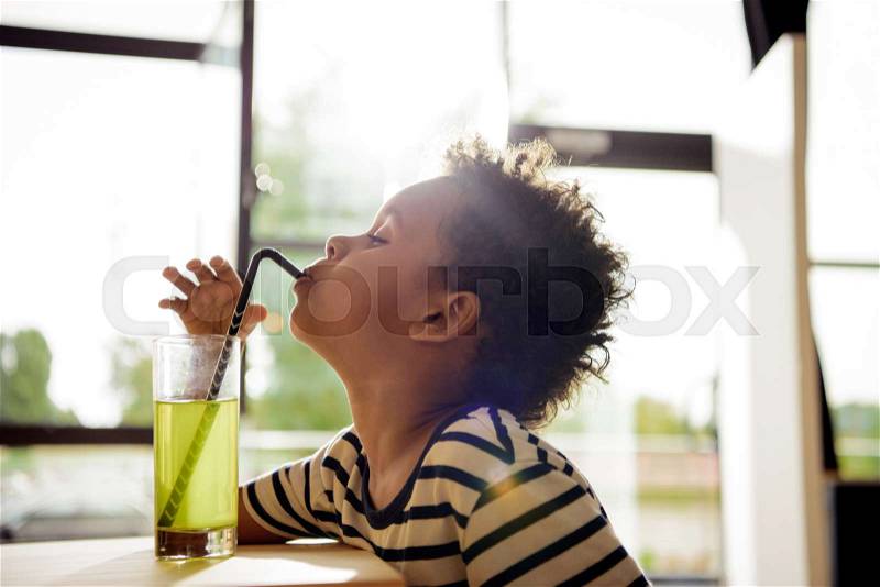 Side view of beautiful african american boy drinking lemonade in cafe, stock photo