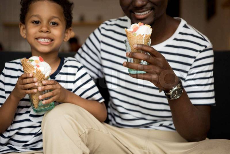 Cropped shot of smiling african american father and son eating ice cream in cafe, stock photo