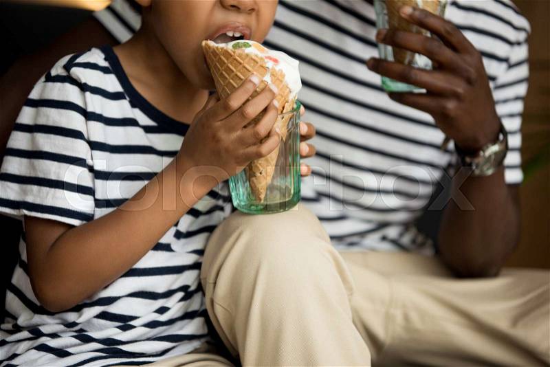 Cropped shot of african american father and son eating ice cream in cafe, stock photo