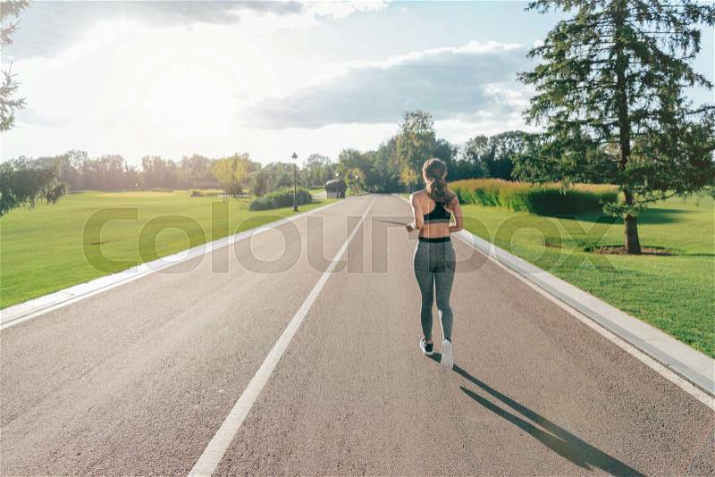 Back view of woman in sportswear running in park alone, stock photo