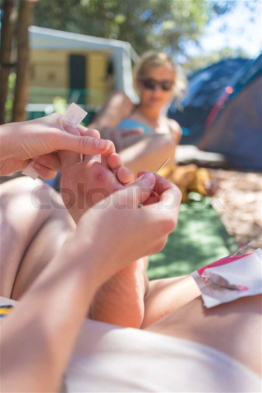 Woman taking spine out of her friends sole using medical needle after she stepped on sea urchin on summer vacations. Improvised domestic first aid, stock photo